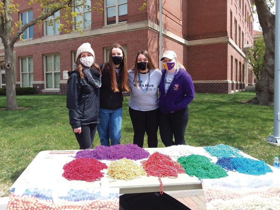 A group of volunteers stand by a table of bead necklaces, each signifying a different way in which suicide has affected peoples lives.